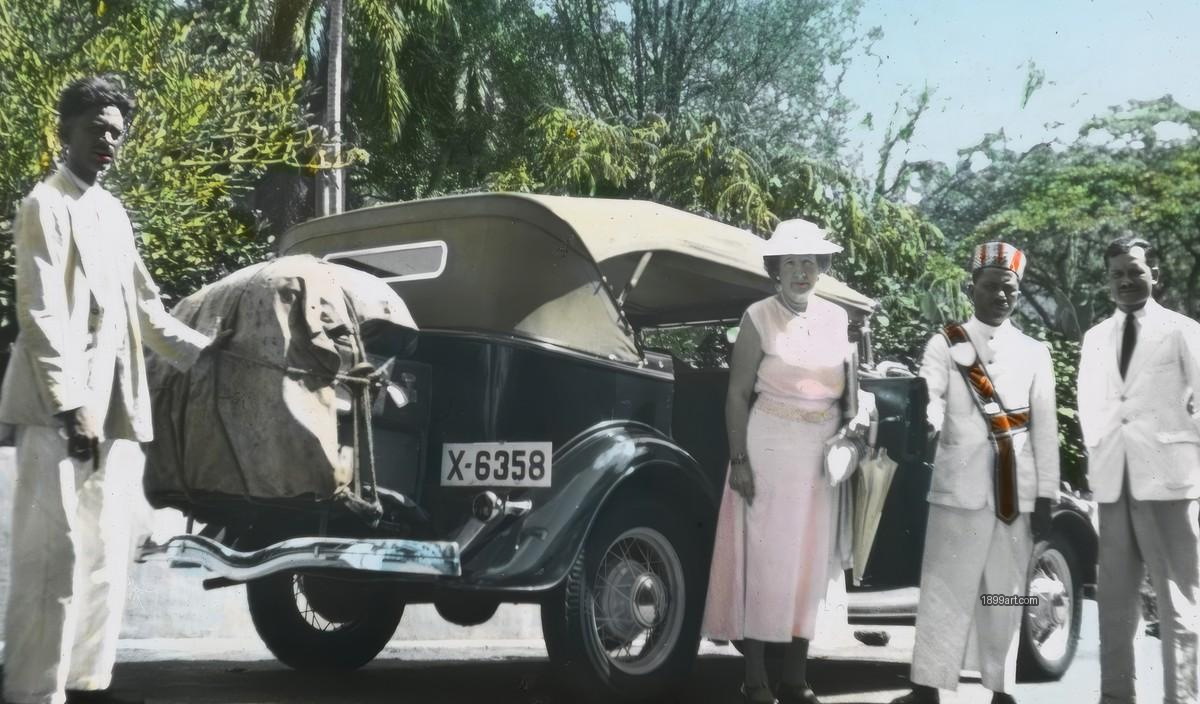 Colonial-era travelers pose beside an early automobile outdoors
