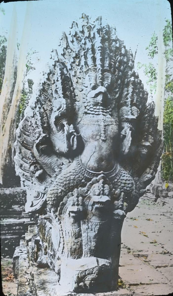 Carved stone multi-headed naga serpent sculpture with trees and ruins