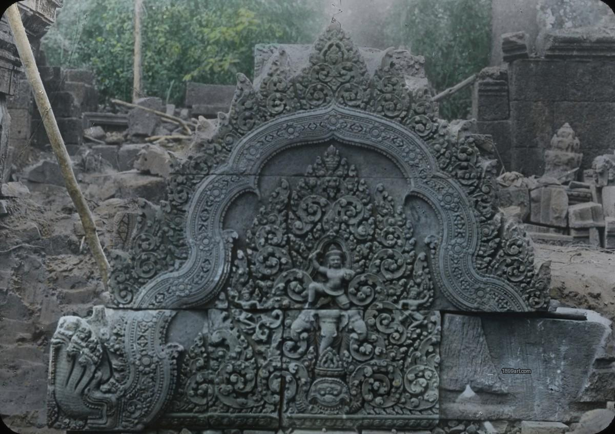 Ornate carved stone lintel with floral motifs amid stones and greenery