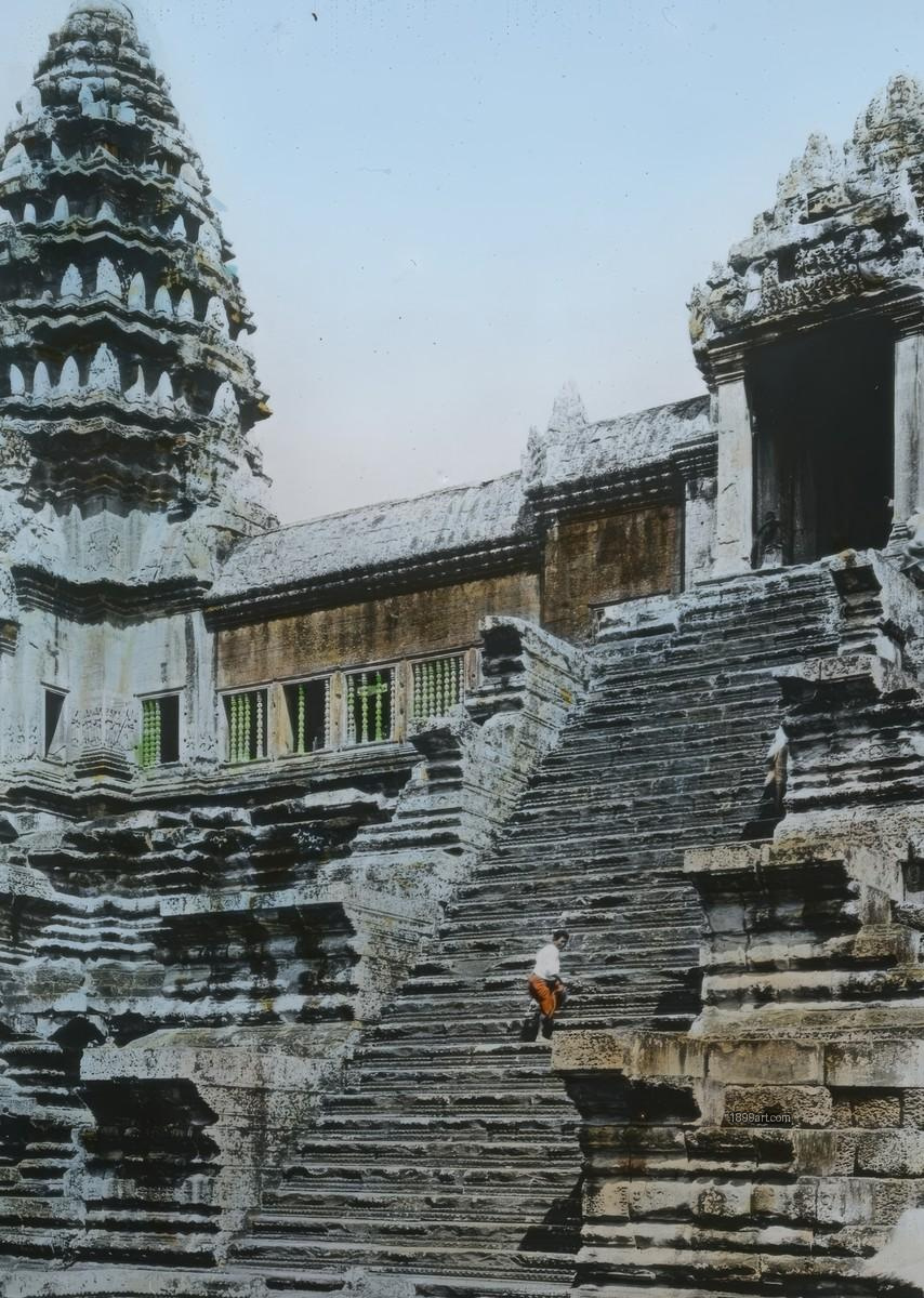 Person in white and orange climbs steep stone steps at Angkor Wat