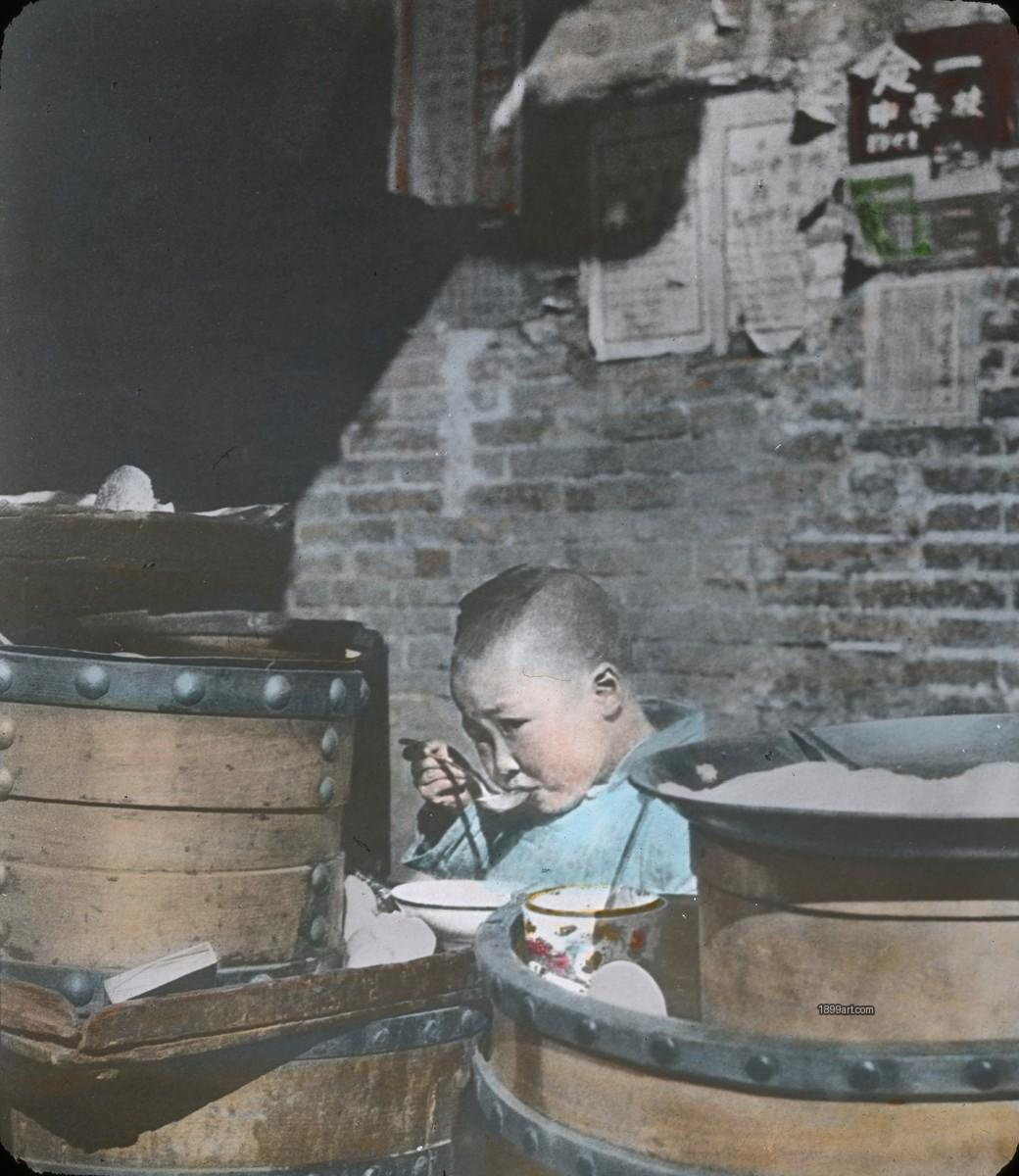 Young boy eating rice soup beside wooden containers against postered brick wall