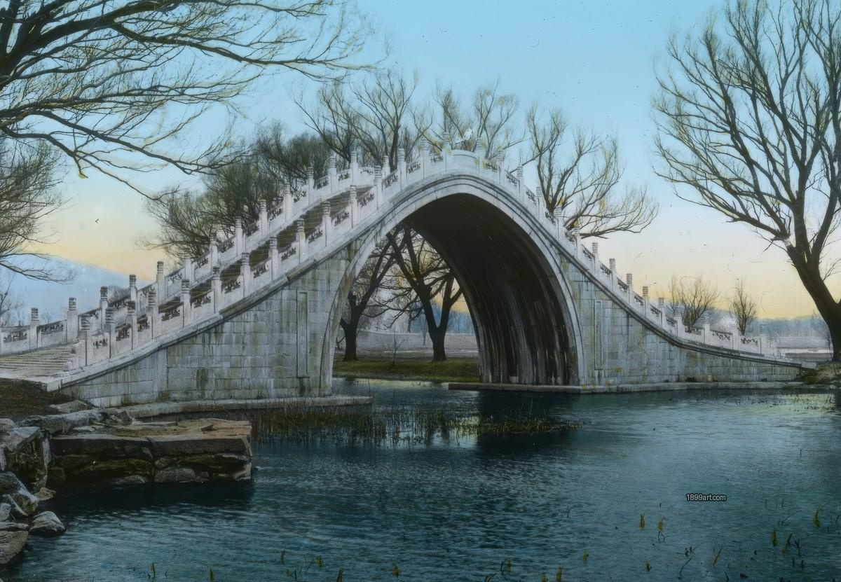 Marble arched stone bridge over calm water with leafless trees
