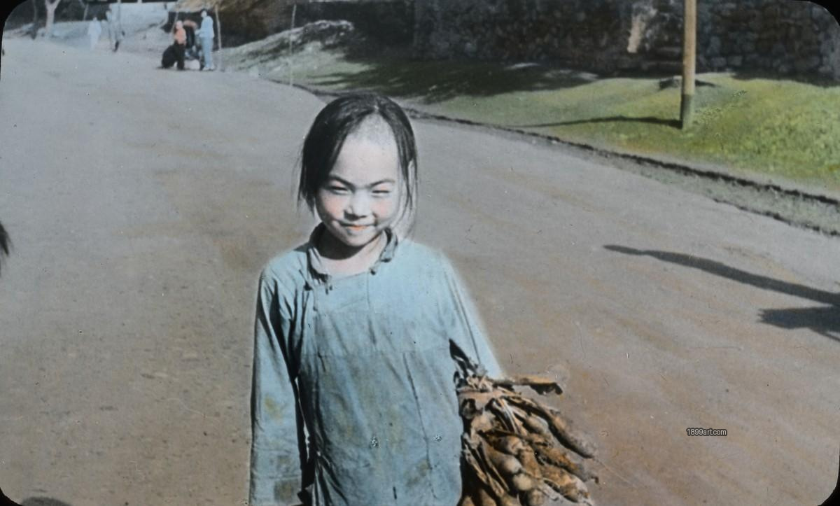 Young girl holding root vegetables on a dirt road beside stone wall