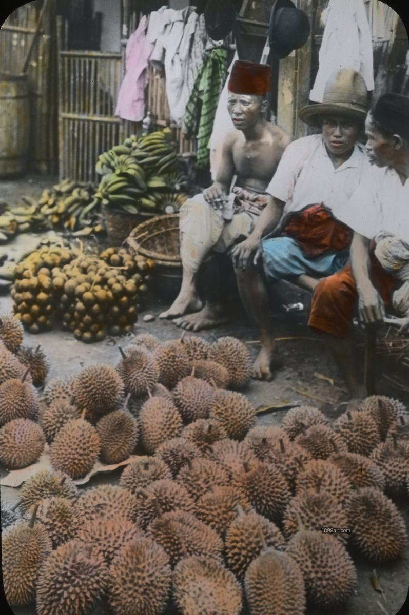 Three men behind durians and fruit baskets with bamboo fence behind
