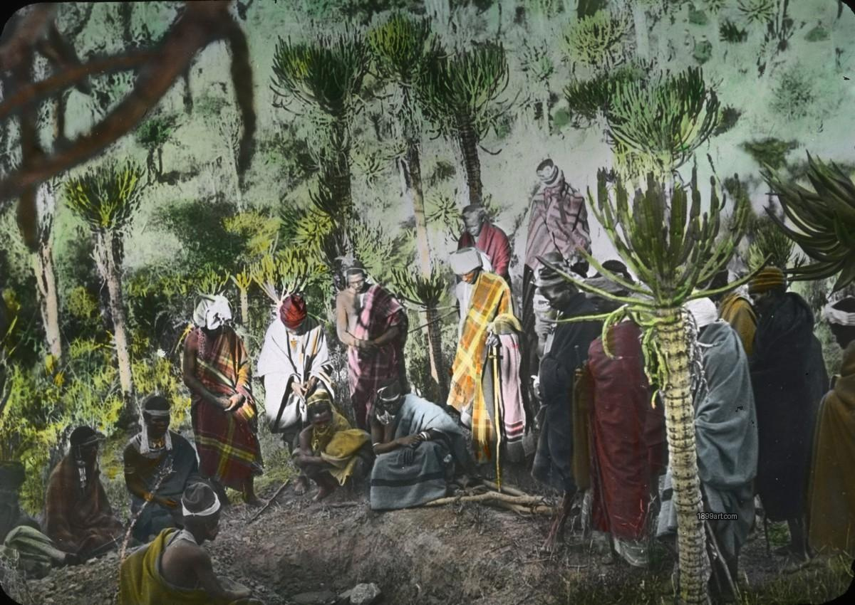 People in traditional clothing gather around a dug hole among trees