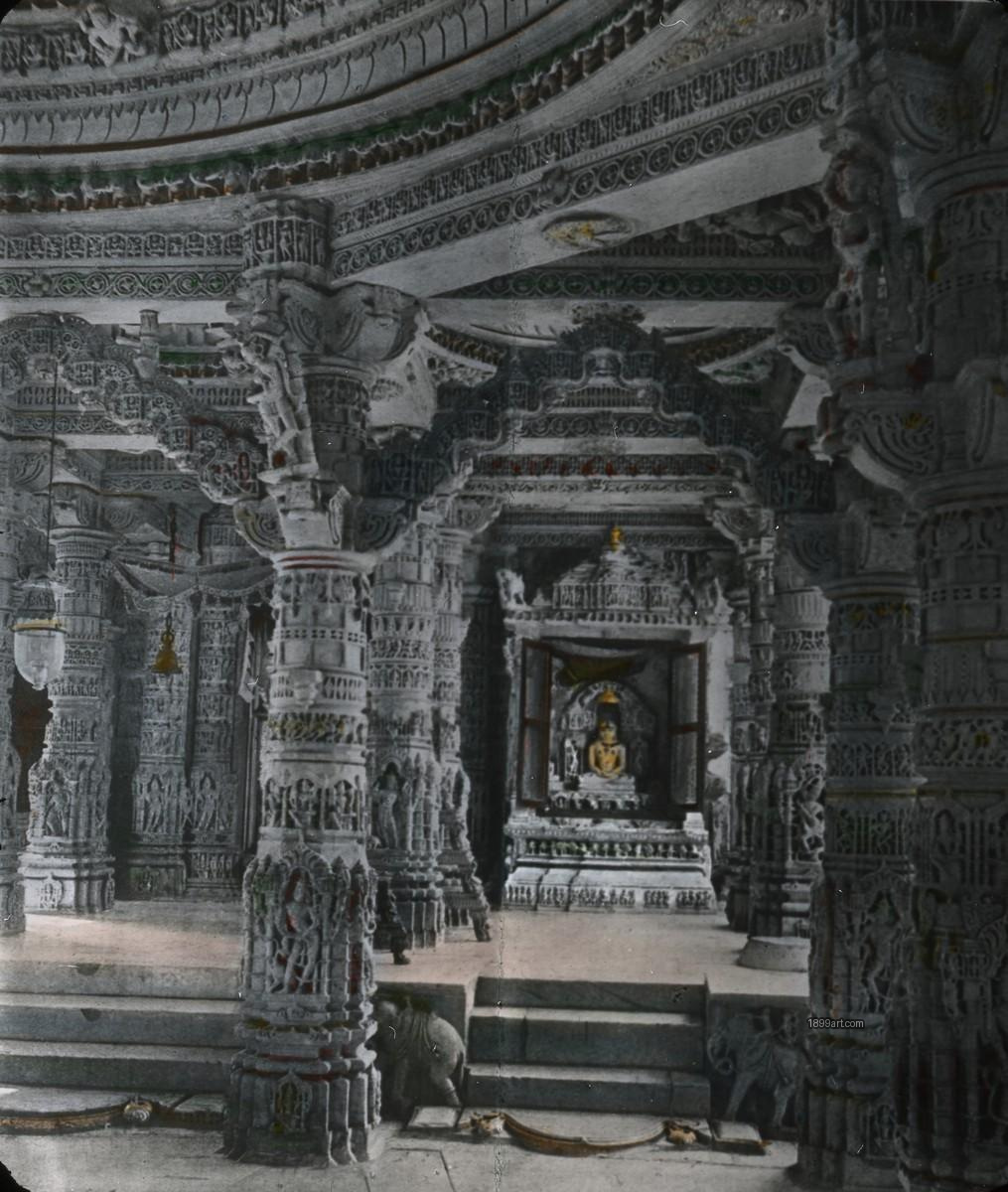 Intricately carved pillars line a temple hall leading to a shrine