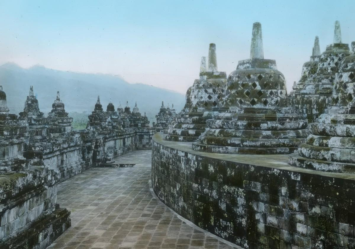 Stone stupas along a curved walkway with mountains and pale sky