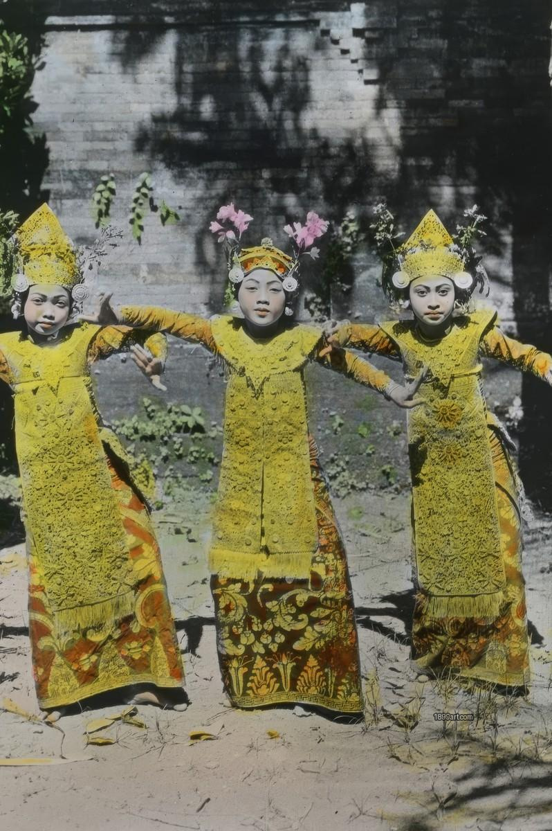 Three children in yellow traditional costumes pose outdoors with arms extended