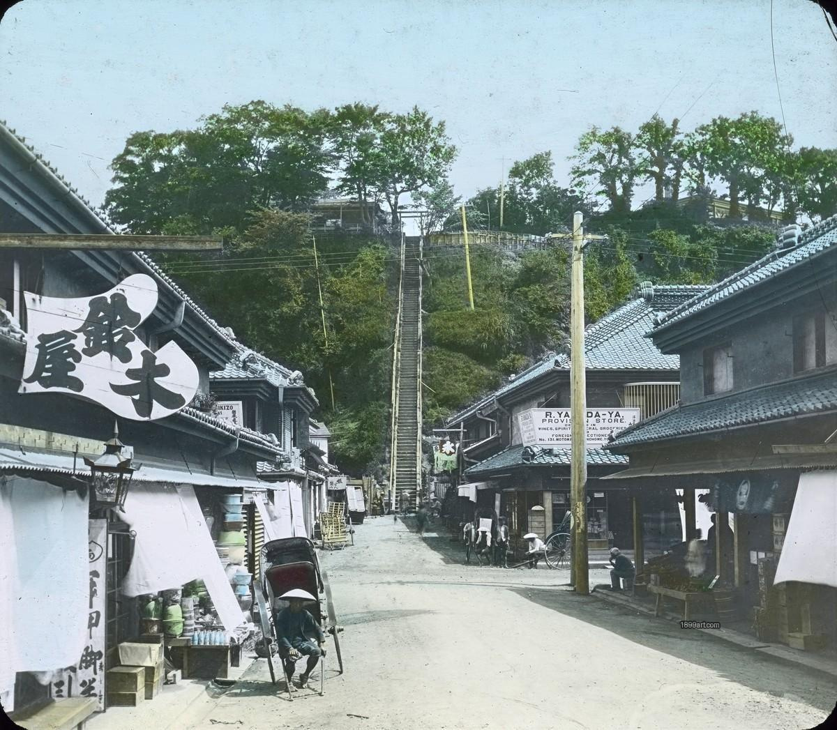 Shop-lined street with rickshaws leading to a large hillside stairway