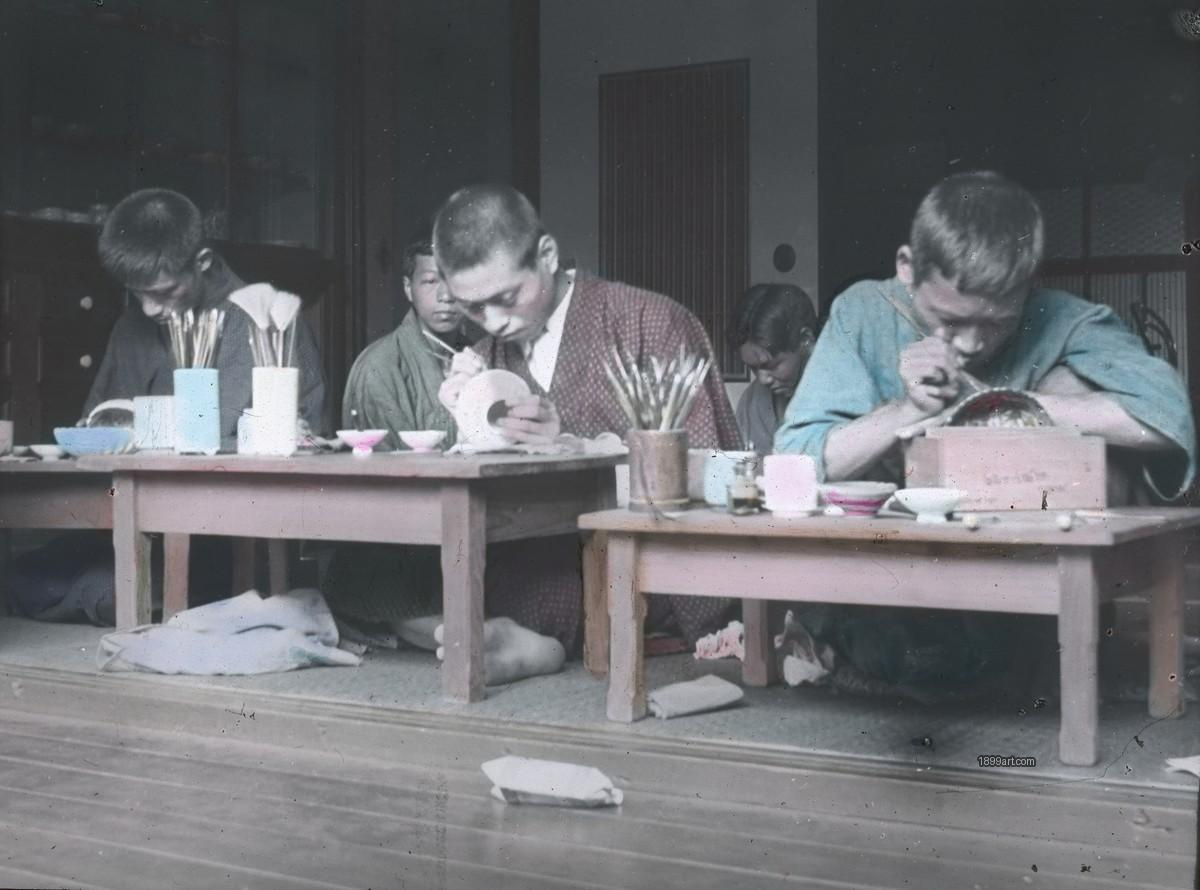 Boys seated indoors paint porcelain at low wooden tables with brushes