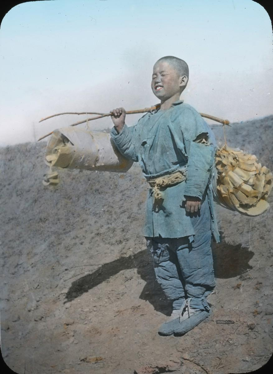 Boy smiles with eyes closed, carrying firewood on shoulder pole