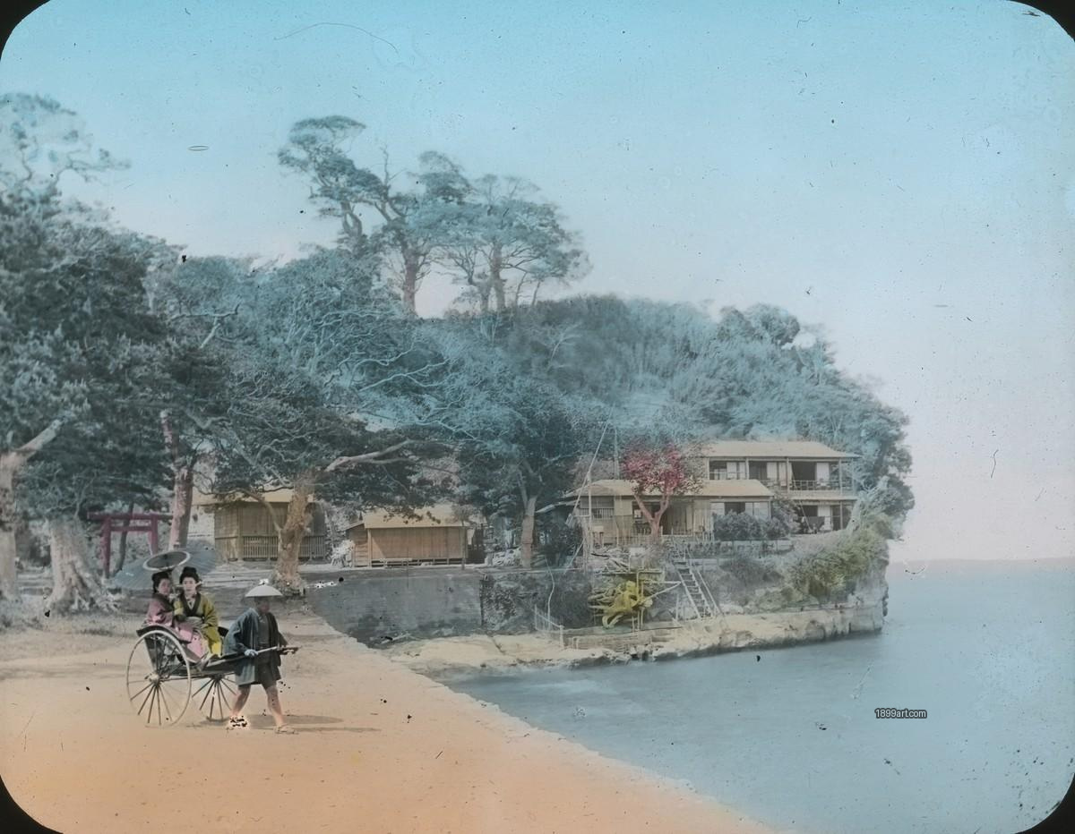 Man pulls rickshaw with two women past coastal wooden buildings