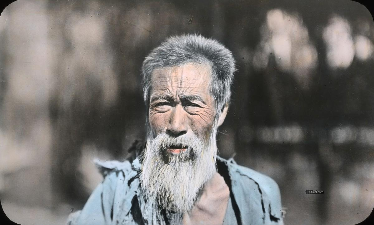 Elderly man with long white beard wearing a tattered garment