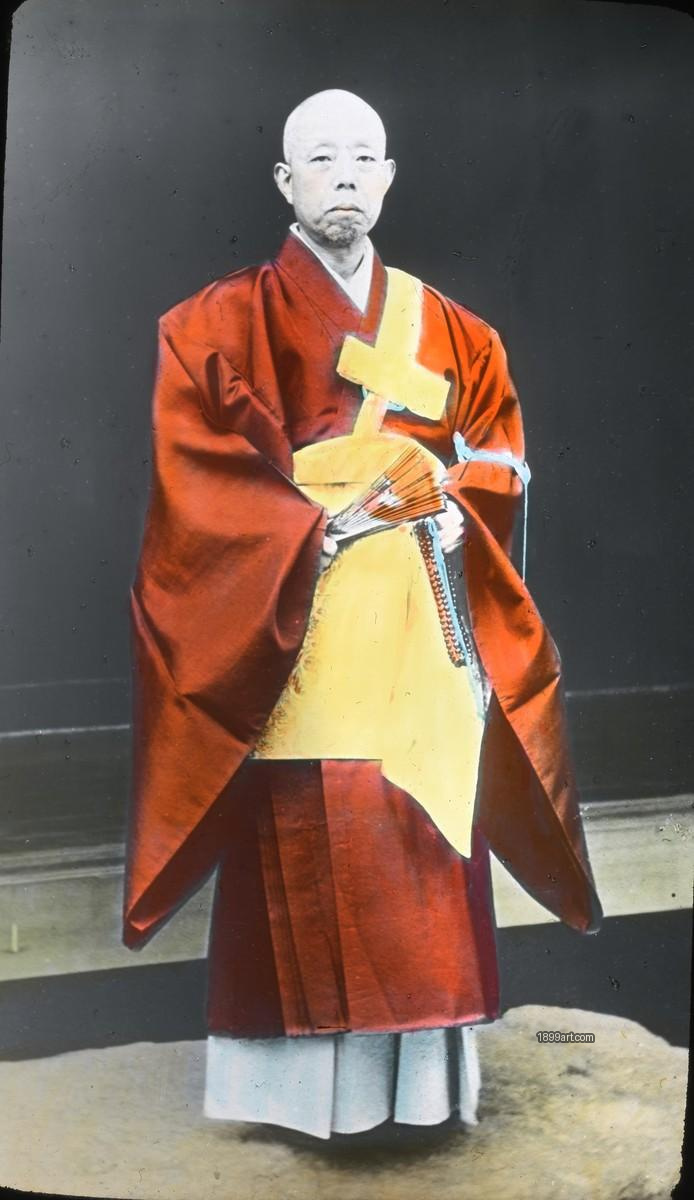 Japanese Buddhist monk in red and yellow robes holding ritual items