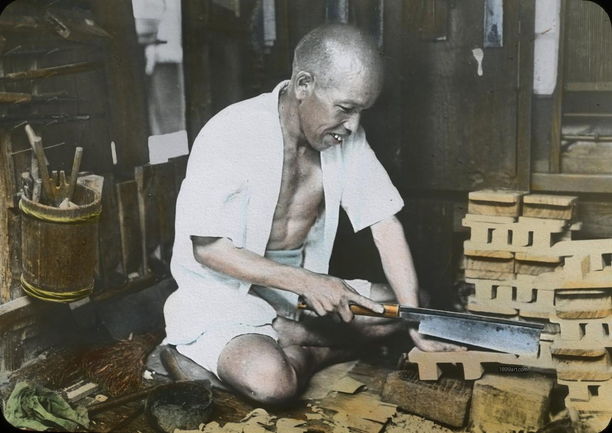 Japanese woodworker sawing a plank on the floor in a workshop