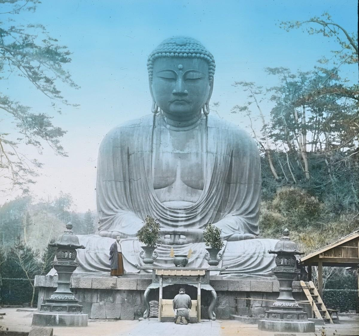 Seated Buddha statue with two visitors, stone lanterns, and trees