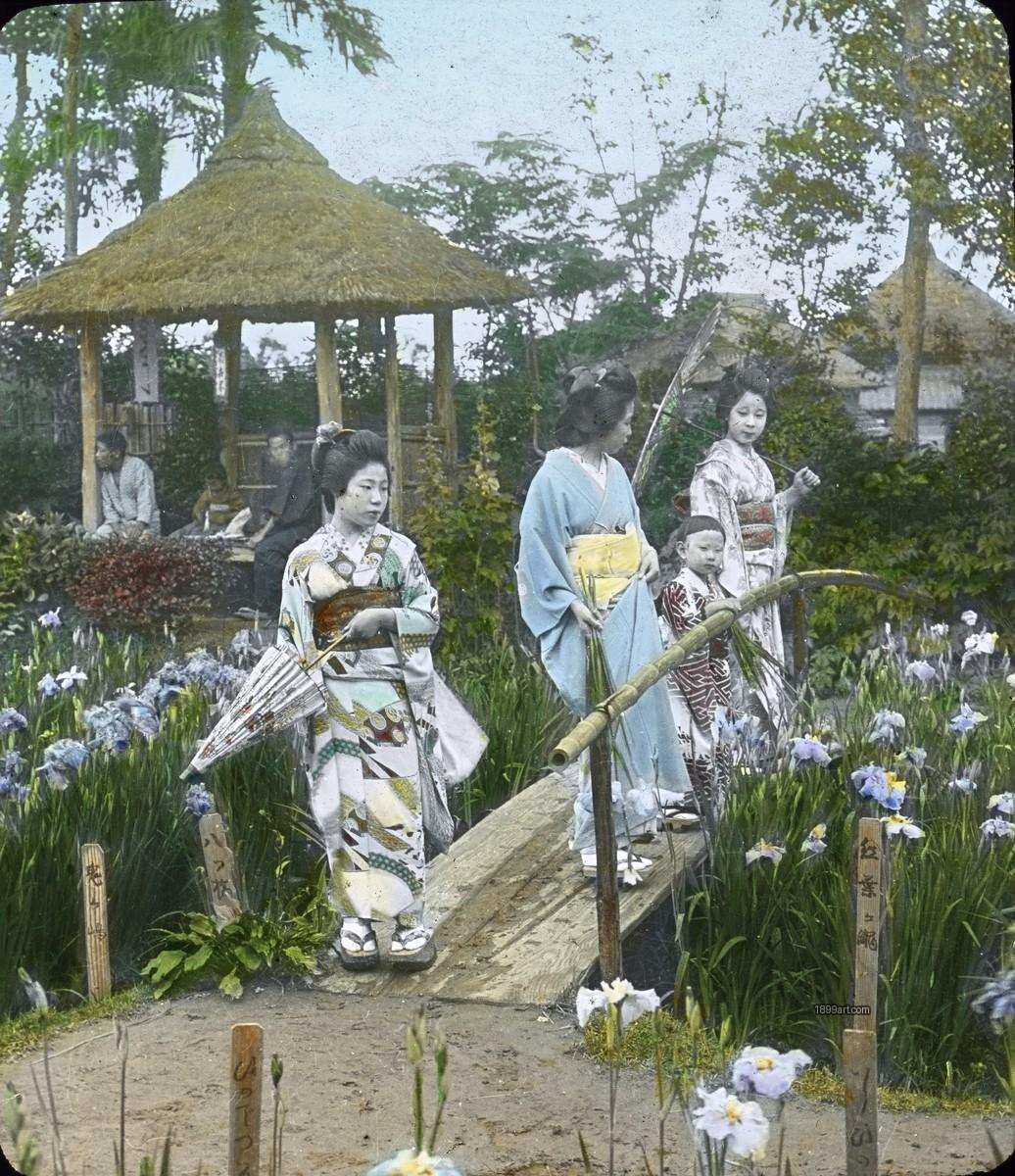 Three women and a child in kimonos cross a wooden bridge