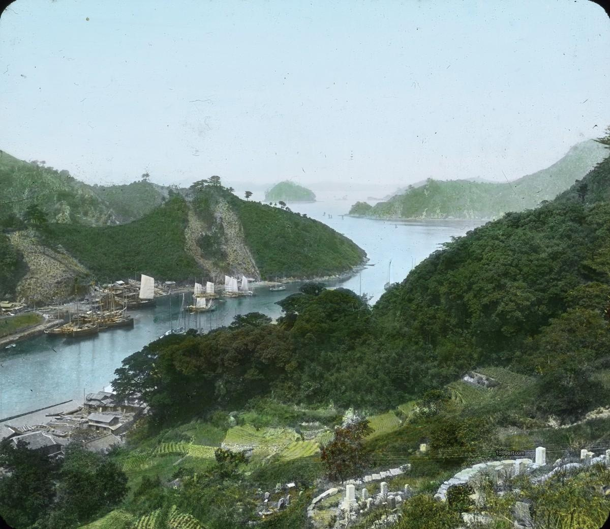 Wide bay with sailing boats, green hills, and fields in foreground