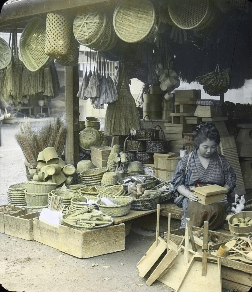 Japanese shop displays baskets and brooms; seated woman holds a wooden box