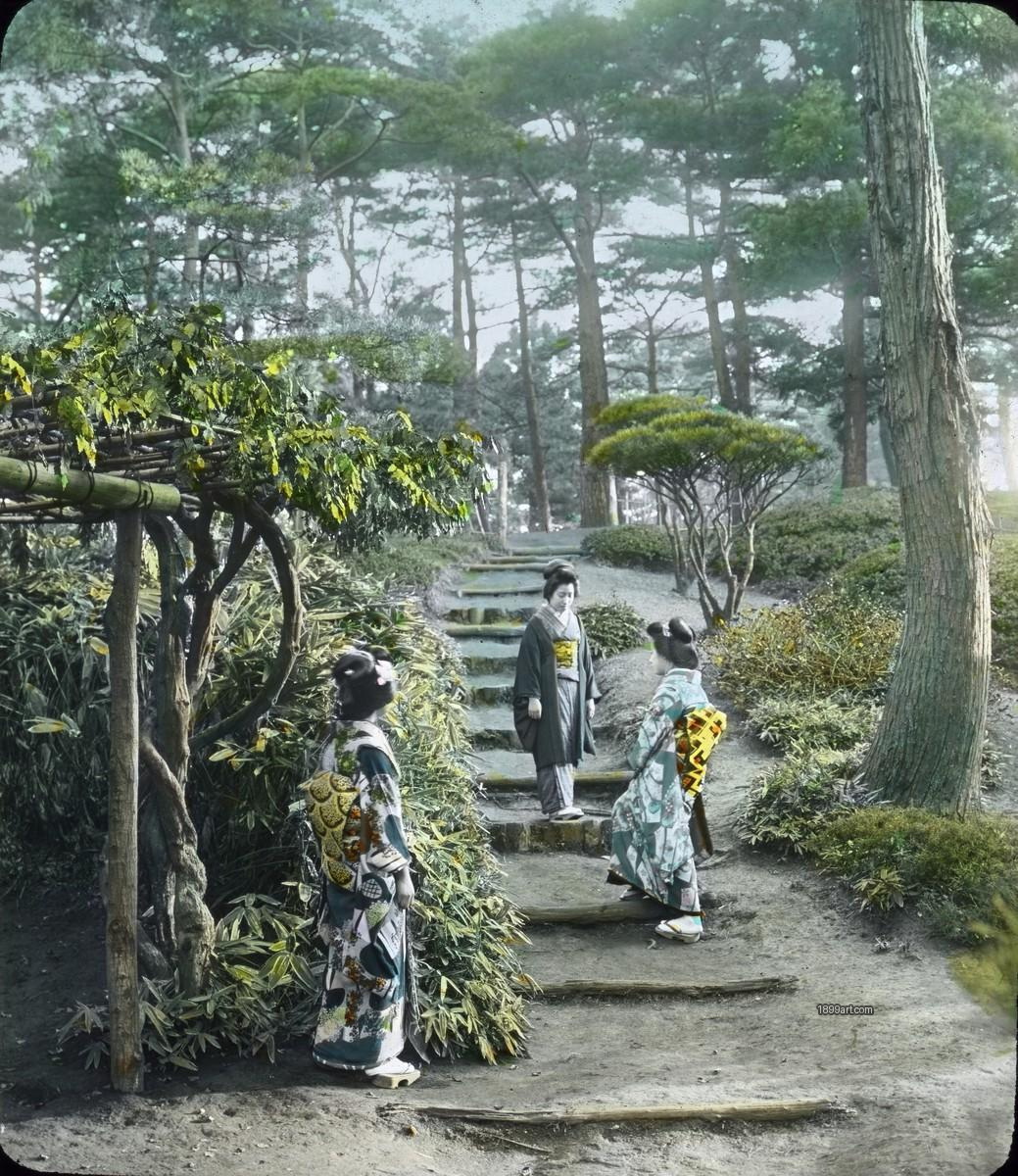 Three women in kimonos stand on a stone path in a garden