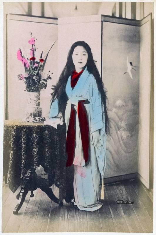 1899art Japan Standing Maiko in Studio Interior with Folding Screen and Floral Arrangement Handcolored 1900s 1899art. Historical photograph from the 1899art Archive.
